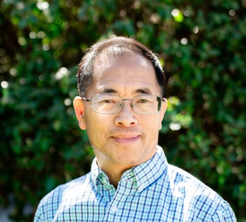 This is a portrait photo of Seng Yang, a board member. He is wearing a collared shirt that has a blue gingham pattern. He has dark, short hair. He has a slight smile and is wearing glasses.