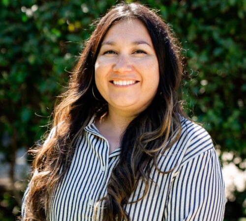 This is a portrait photo of Vanessa Guerra. She is wearing a striped black and white collared shirt and is smiling.