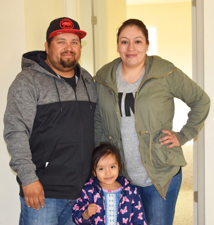 A husband and wife stand with their young daughter inside the home that the family built with the help of CHIP. In the background, you see a doorway to an empty bedroom that is light and bright.