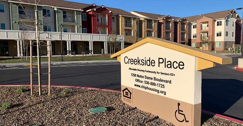 An image of Creekside Place Apartments on a sunny morning shows the front east wing behind a large monument-style sign that reads "Creekside Place."