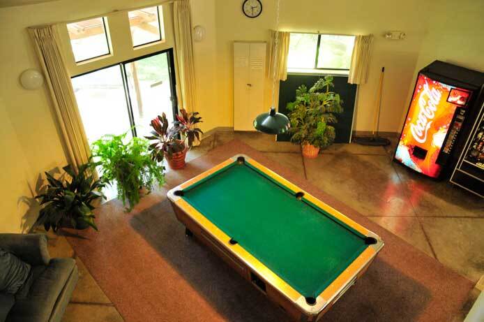 The photo shows a pool table from a vantage point above it. There is a soda vending machine against one of the walls. There is a window and a sliding glass door window.