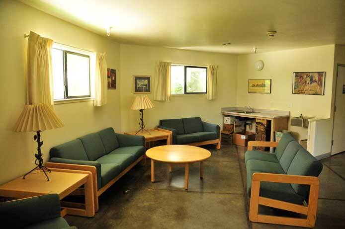 The photo shows another community space with three sofas and a coffee table. There are two windows with drapes and two side tables with one on each table.