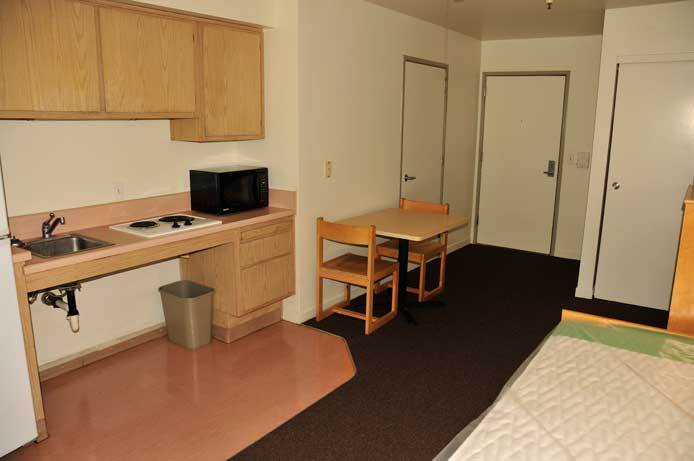 A photo of one of the units at Campbell Commons. It shows a studio unit with a kitchenette that has a sink, a stovetop, and a microwave oven. A two-person dinning table is near the kitchenette.